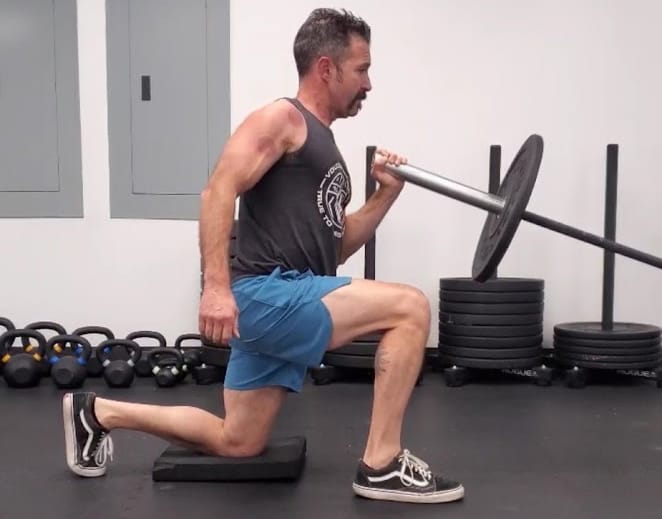 A weight lifter on one knee lifting a barbell with one hand doing an excercise.