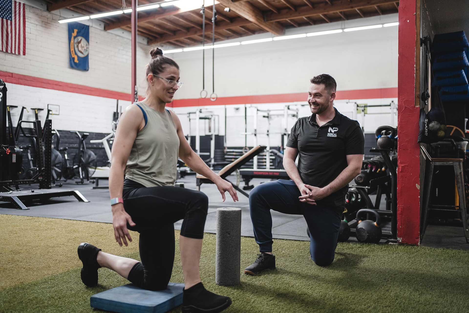 A person in a gym on one knee with a physical trainer